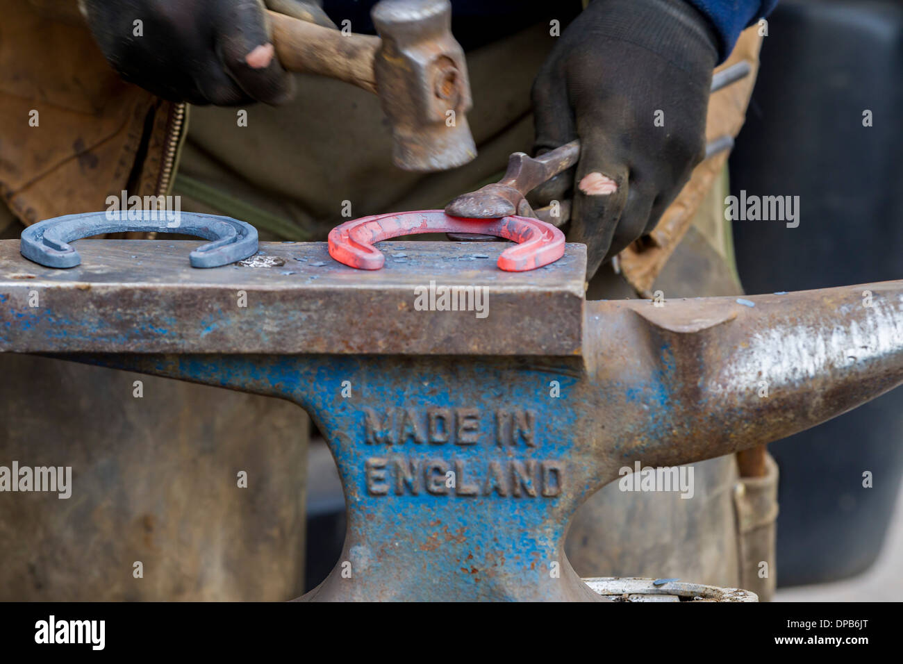 Farrier hammering red hot glowing horseshoe on anvil. Stock Photo