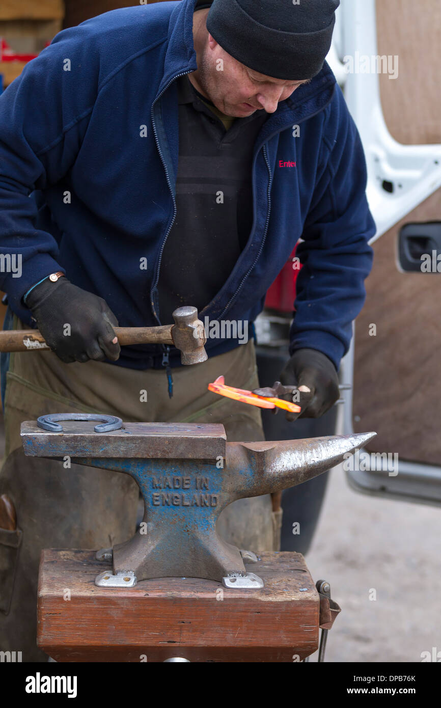 Farrier hammering red hot glowing horseshoe on anvil Stock Photo