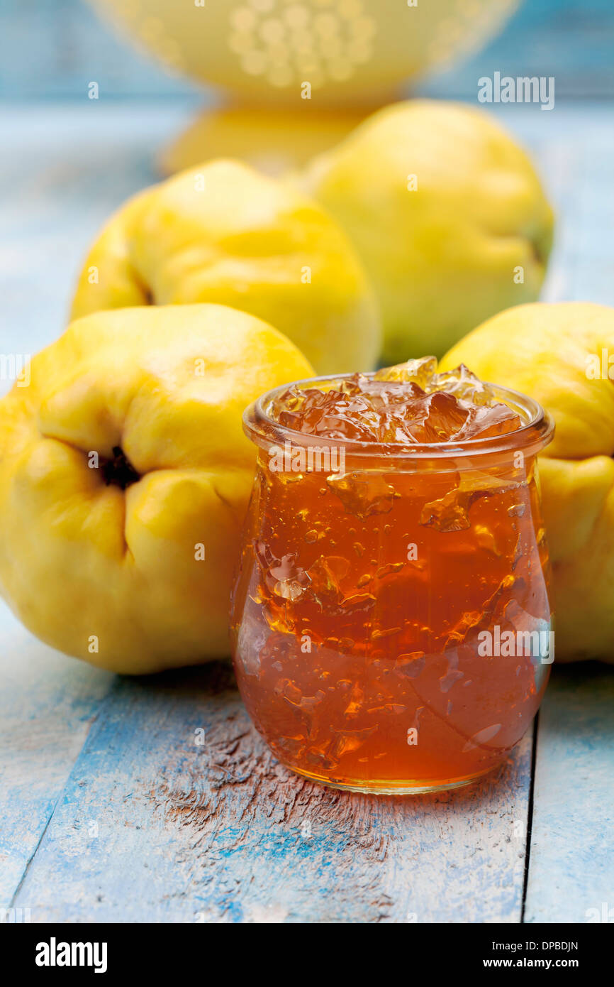 Four quinces (Cydonia oblonga), a spoon and a glass of quince marmalade on wooden table Stock
