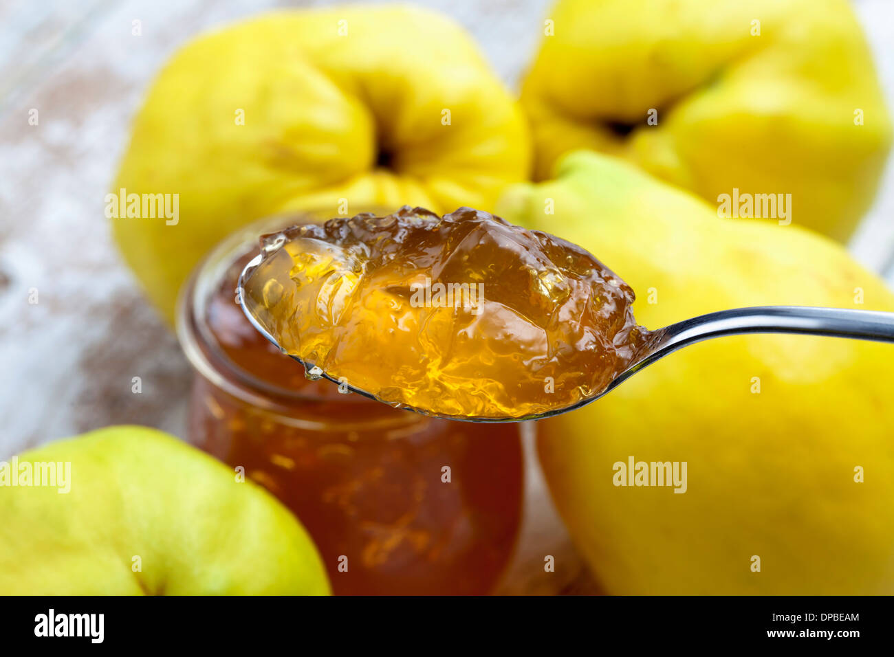 Four quinces (Cydonia oblonga), a spoon and a glass of quince marmalade on wooden table Stock