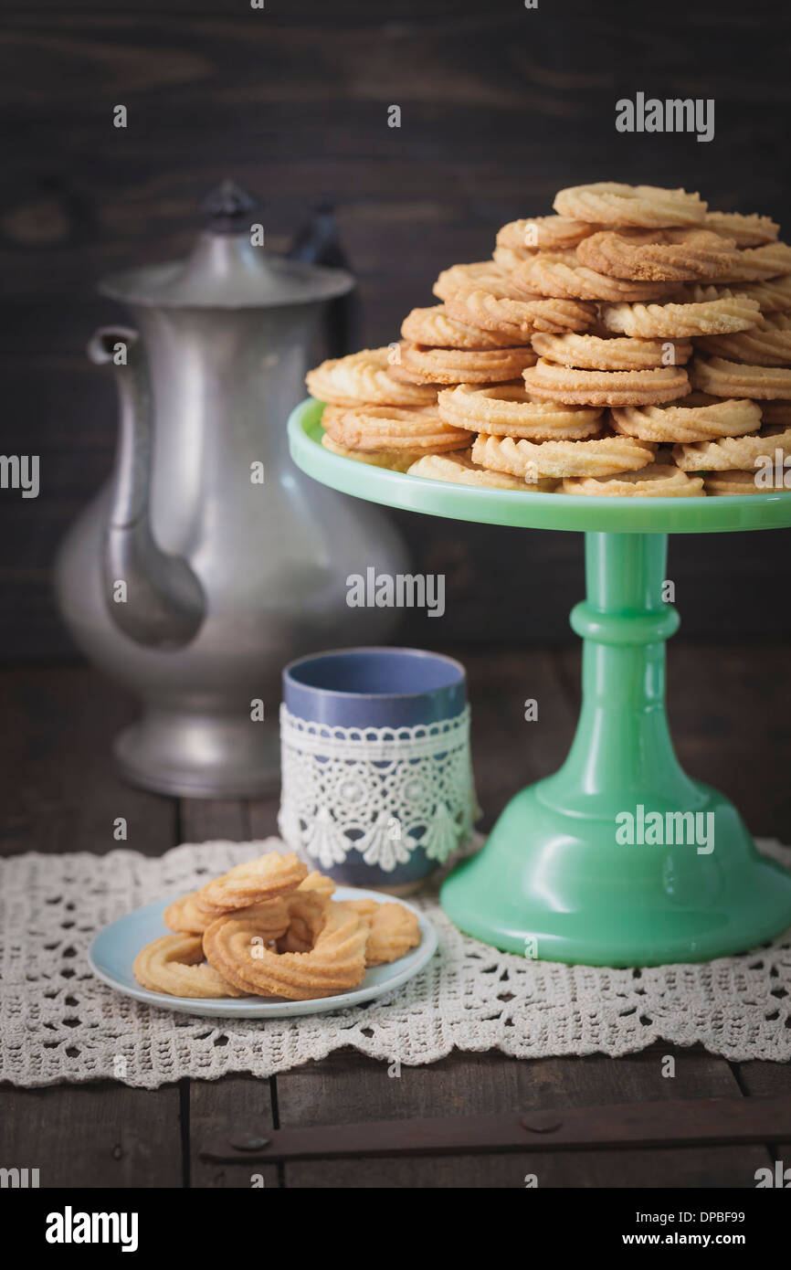 Traditional spritz cookies on green cake plate and coffeepot in background<br /> Stock Photo