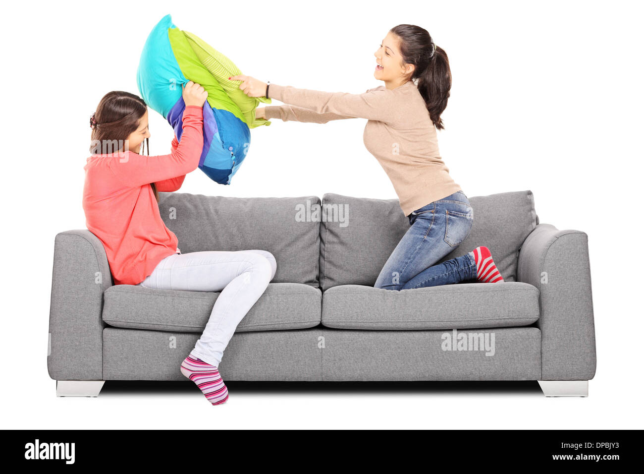 Two young girls having a pillow fight seated on sofa Stock Photo