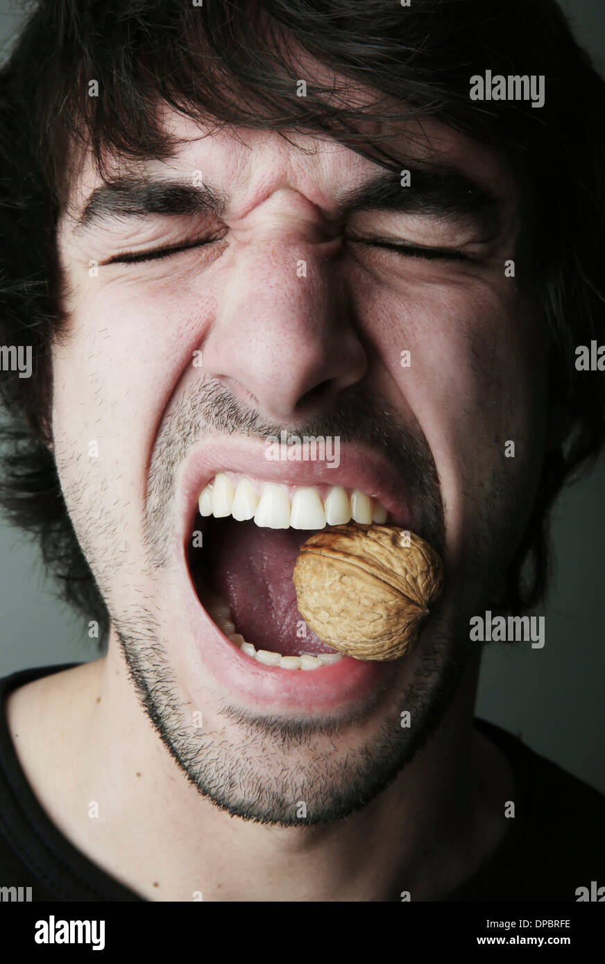 Portrait of young man trying to crack a walnut with his teeth, studio shot Stock Photo