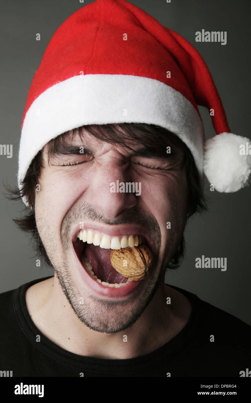 Young man with Santa hat trying to crack a walnut with his teeth, studio shot Stock Photo