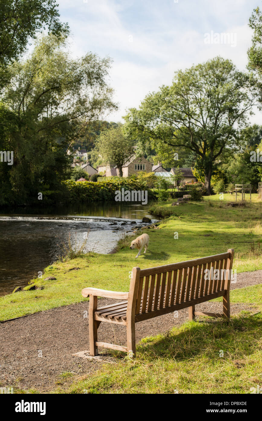 Country rustic bench overlooking stream of water in Bakewell, Derbyshire, UK Stock Photo