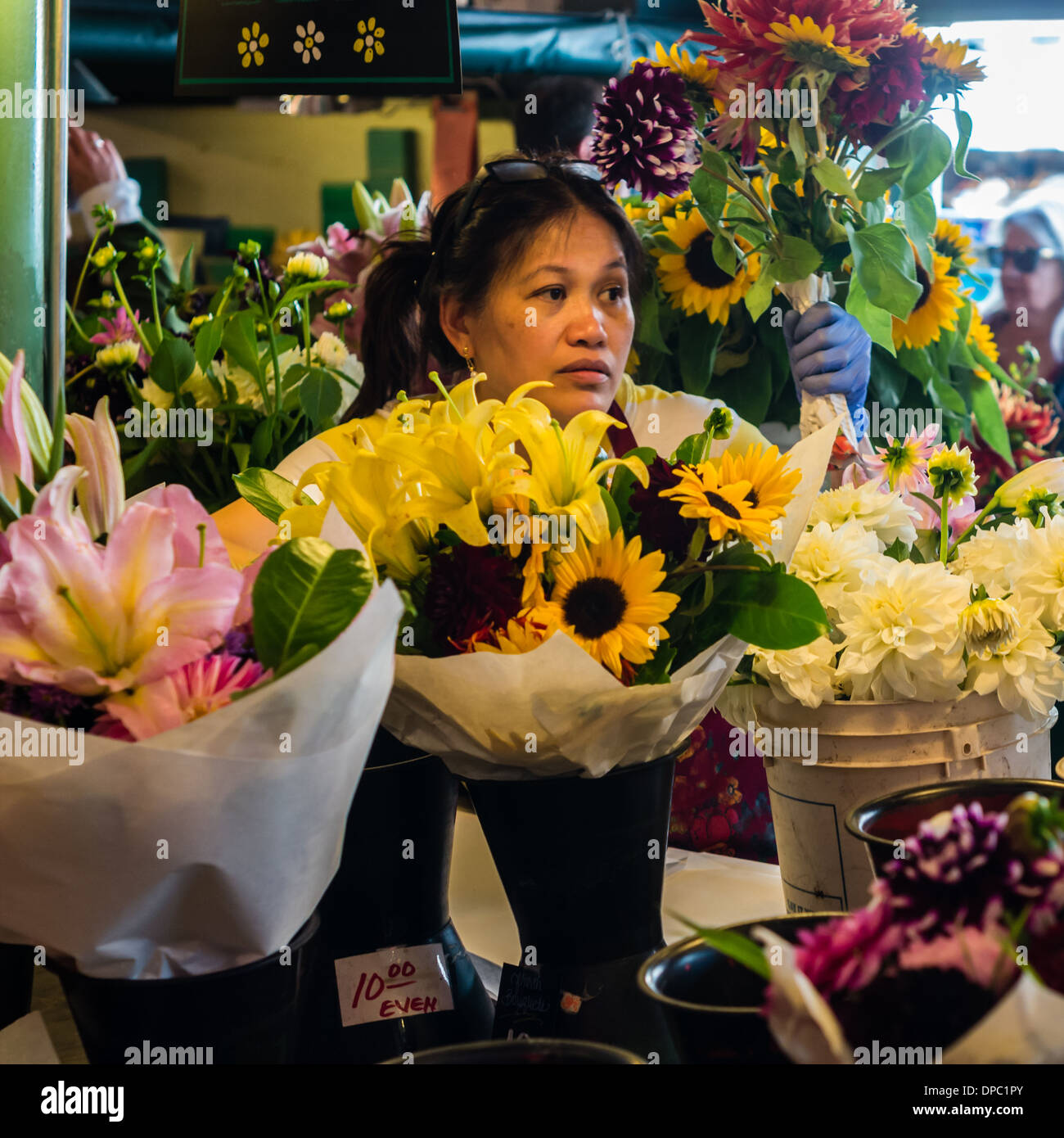 Flower seller with bouquet of flowers and tubs of fresh flowers at a market stall.  Pike Place Market, Seattle, Washington, USA Stock Photo