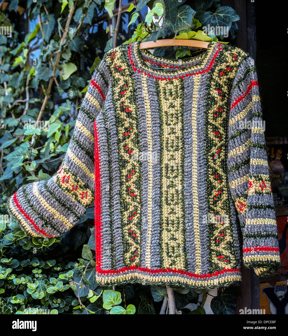 A handmade long-sleeve sweater that was crocheted in several patterns with multicolored yarn is displayed against an ivy plant in California in 1976. Stock Photo