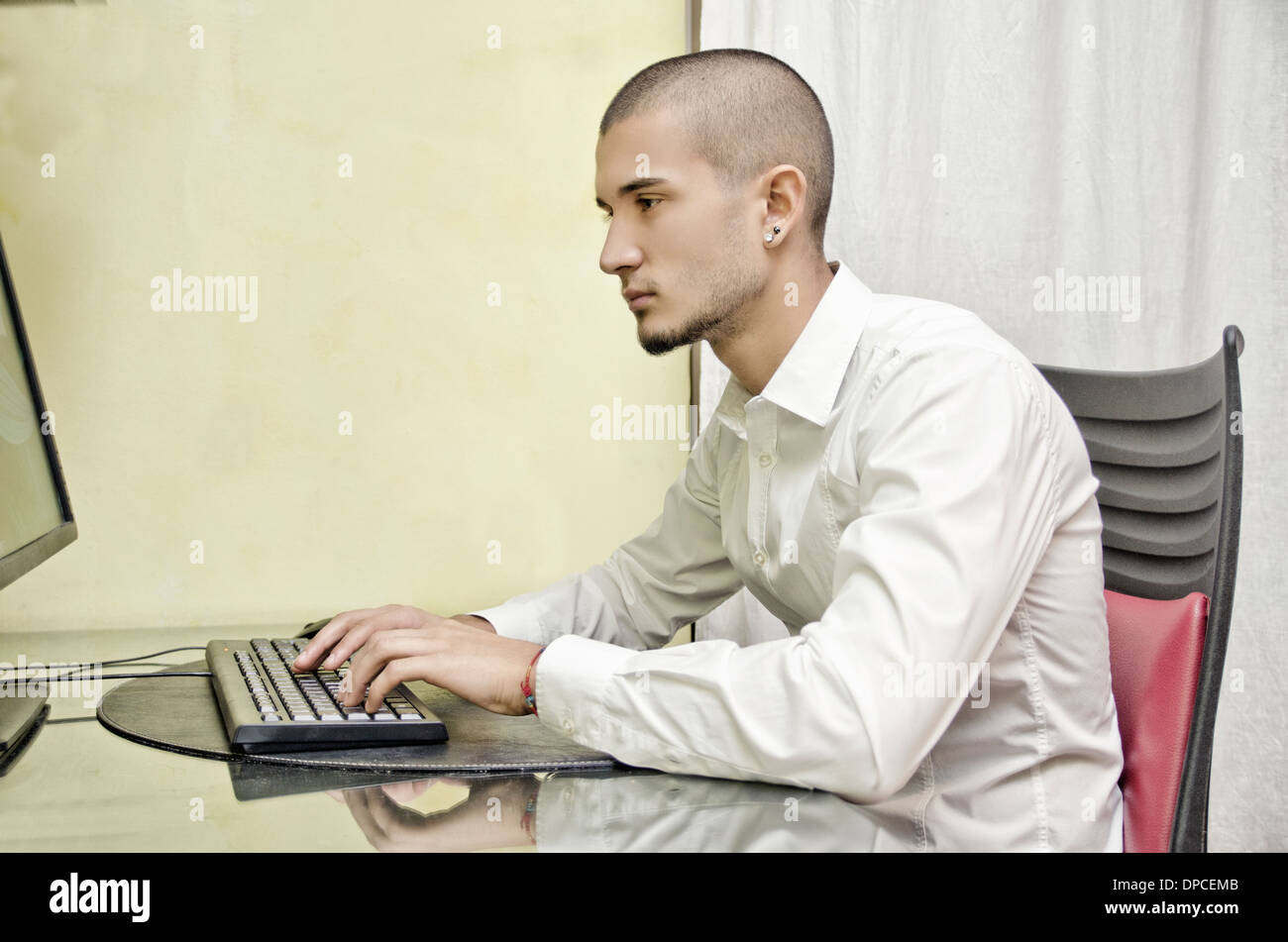 Attractive young man at home sitting at desk, working with computer Stock Photo