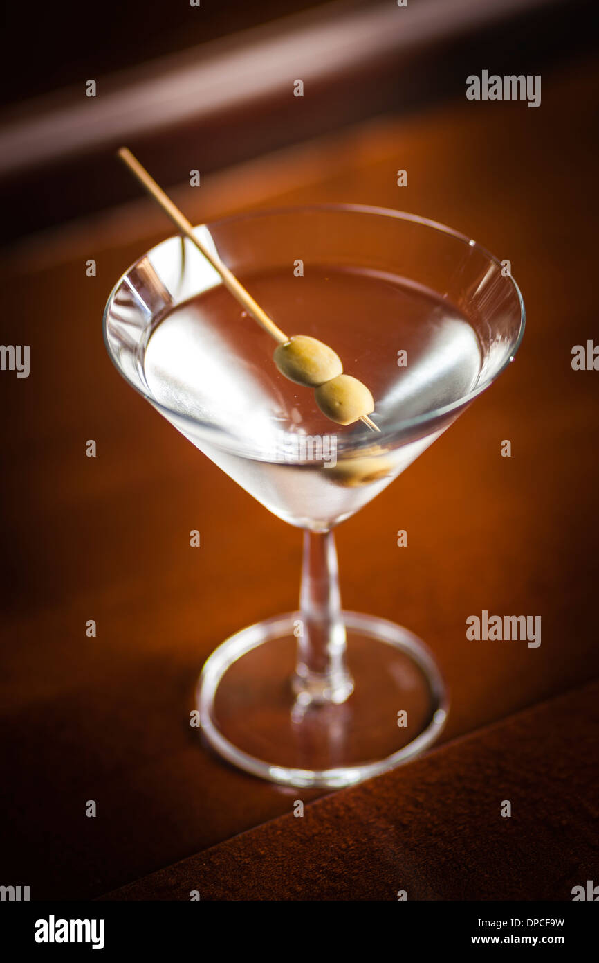 One glass of famous Classic Cocktail Dry Martini with Olive, shot on location on wooden Bar. Stock Photo