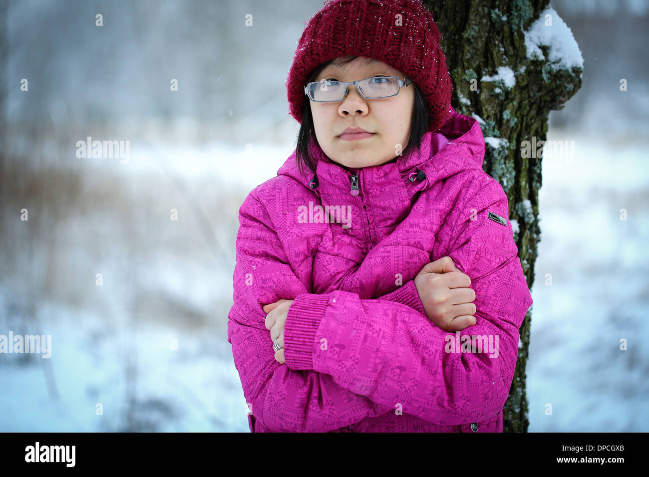 Young and moody asian girl with a pink jacket leaning against a tree in the winter Stock Photo