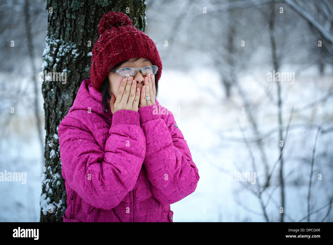 Young and moody asian girl with a pink jacket leaning against a tree in the winter Stock Photo