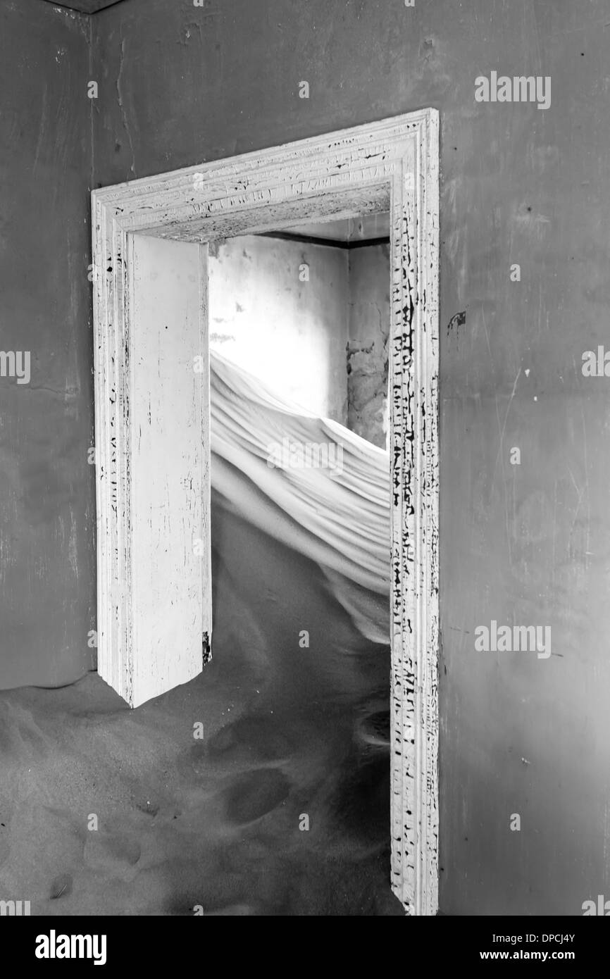 Interior doorway into room filled with sand dune in abandoned house of former mining town now a ghost town in Namibia Stock Photo