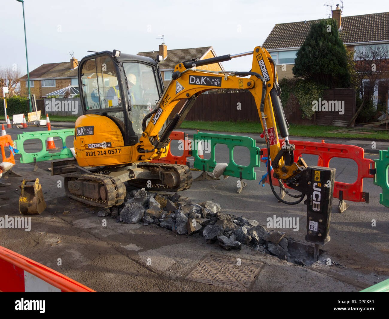 A JCB mini excavator fitted with an hydraulic pick excavating a trench for renewal of a water main pipe Stock Photo