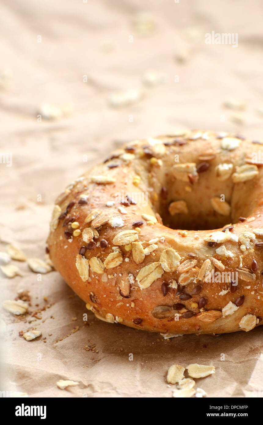 Multi-grain bagel covered in oats and seeds on crinkled brown paper Stock Photo