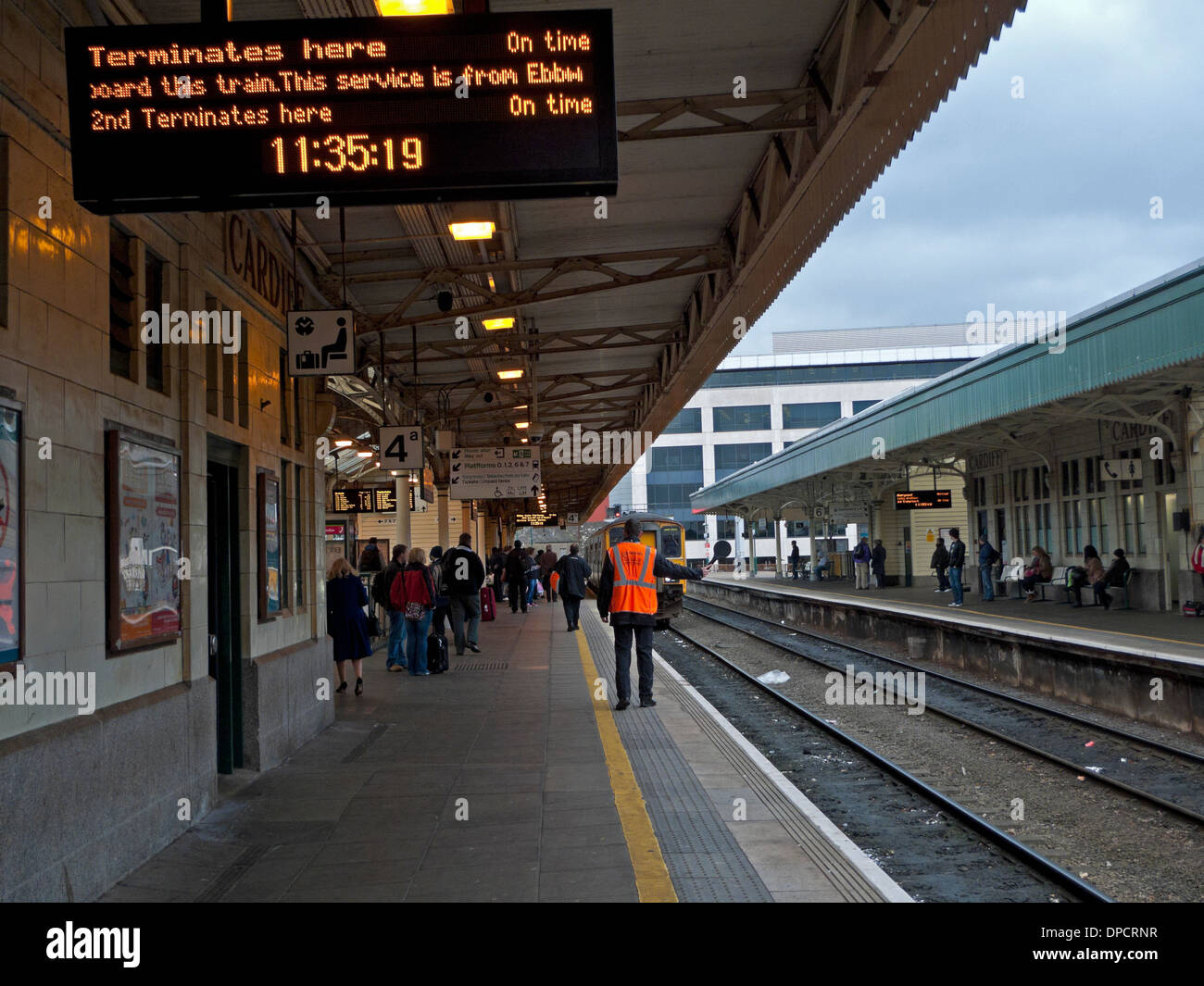 Electronic display and guard on platform with train approaching Stock