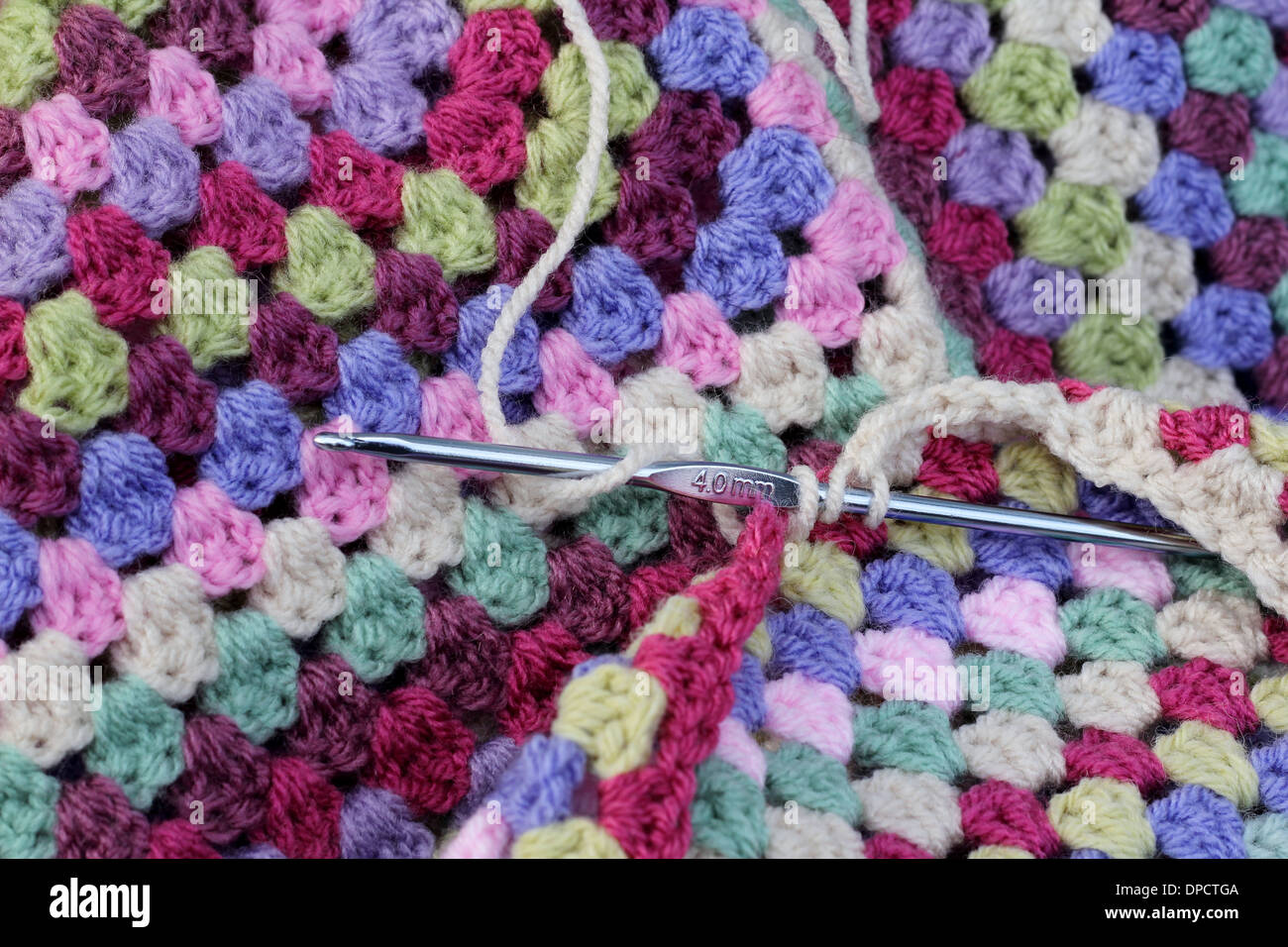 Crochet hook being used to crochet a hand made afghan blanket, colors are pink, blue, purple, green, shabby chic , retro hobby Stock Photo