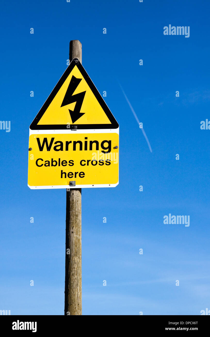 Yellow and black warning sign marking where cables cross under a river. An airplane trail is seen in the sky. Stock Photo