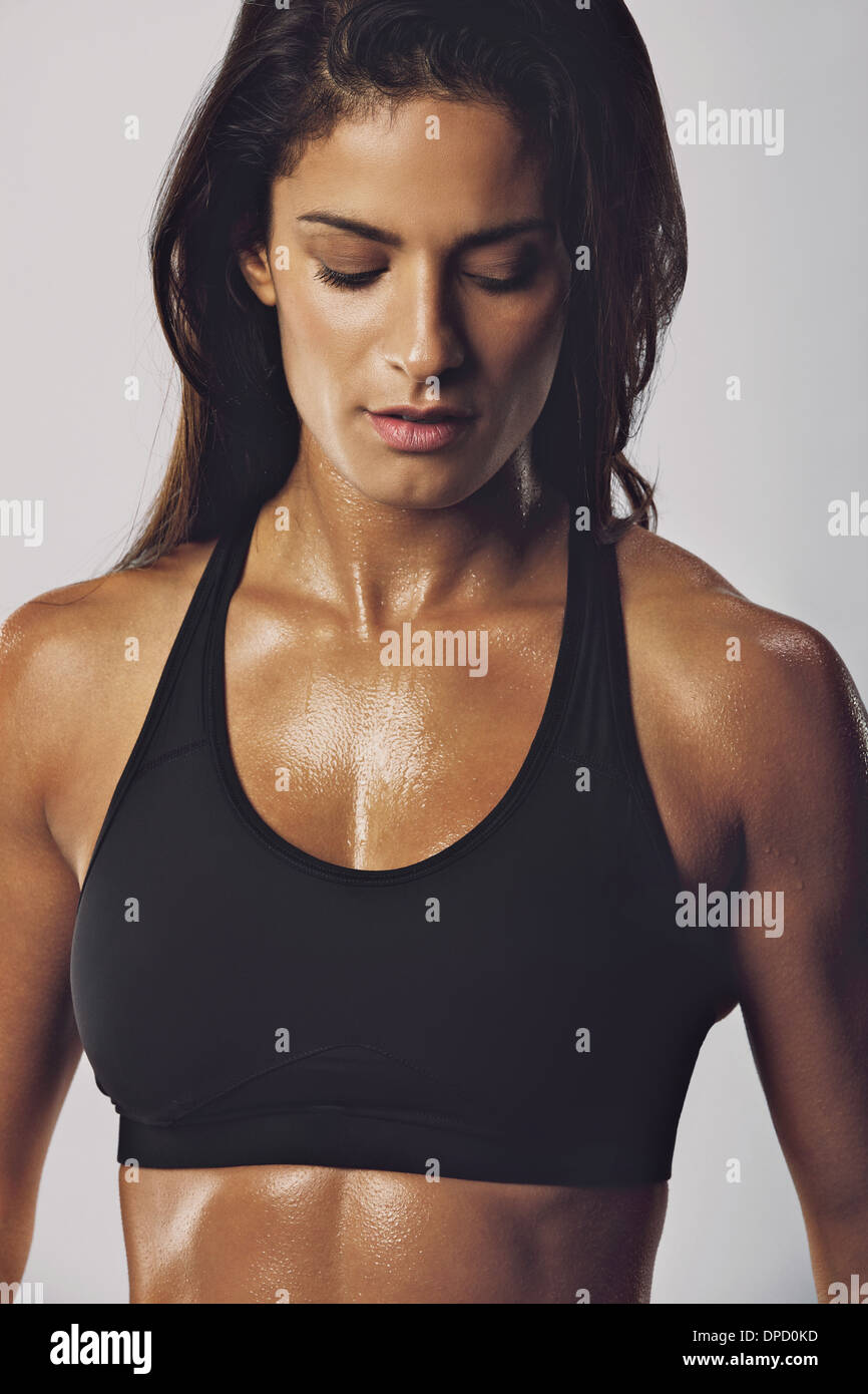 Portrait of middle eastern woman in sports bra with muscular body looking down against grey background. Female bodybuilder model Stock Photo