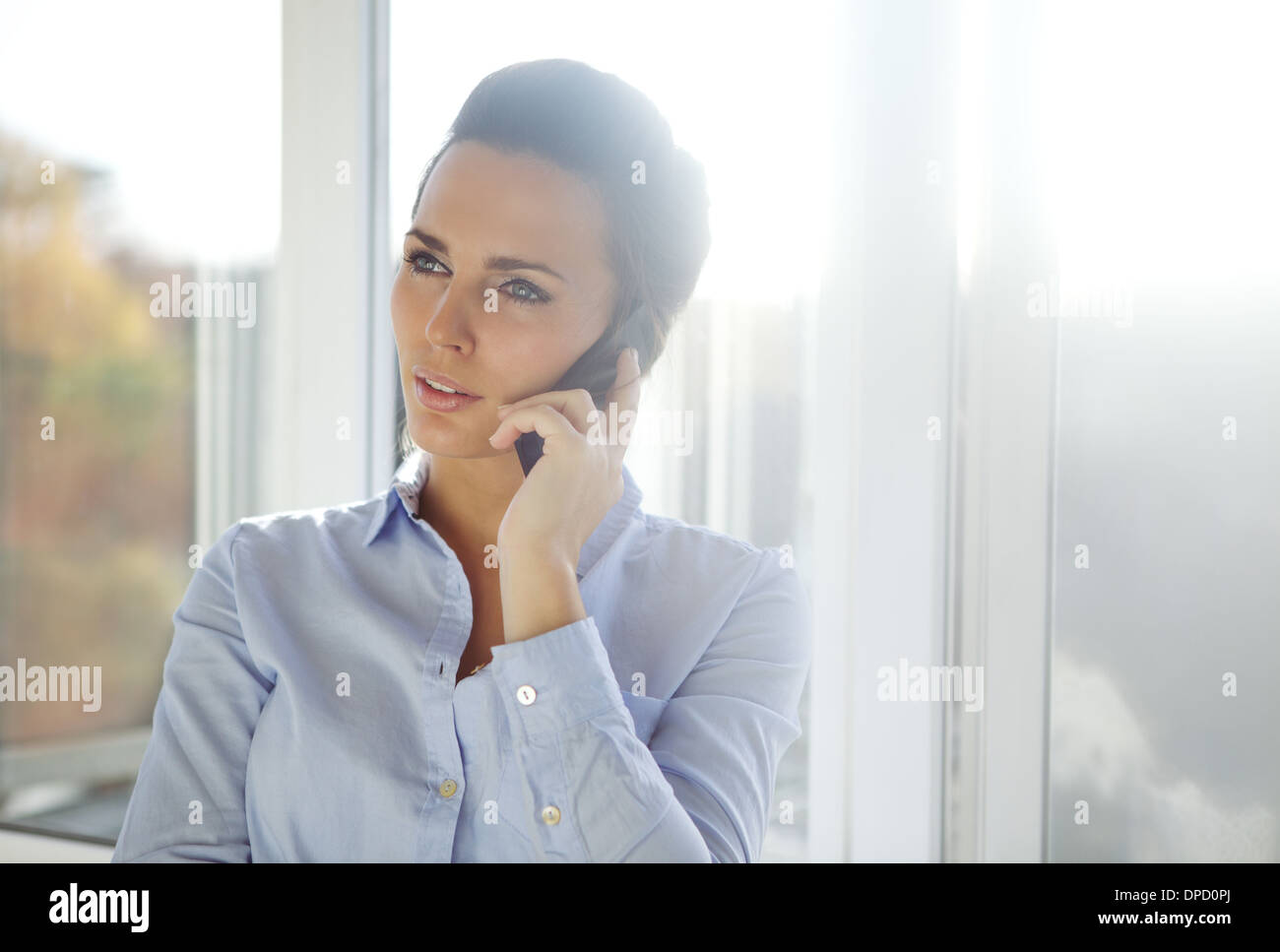 business woman standing in a bright office while talking on her mobile phone looking away. Beautiful caucasian female model Stock Photo