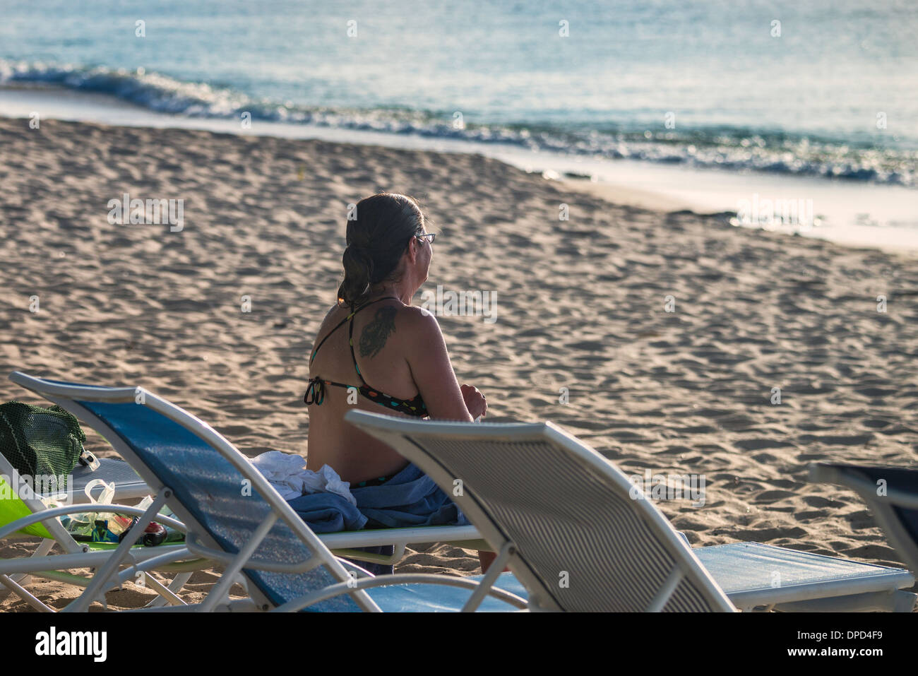A woman in her early 40s sits on Sandcastle beach in her bathing suit and looks out to sea in St. Croix, U.S. Virgin Islands. Stock Photo