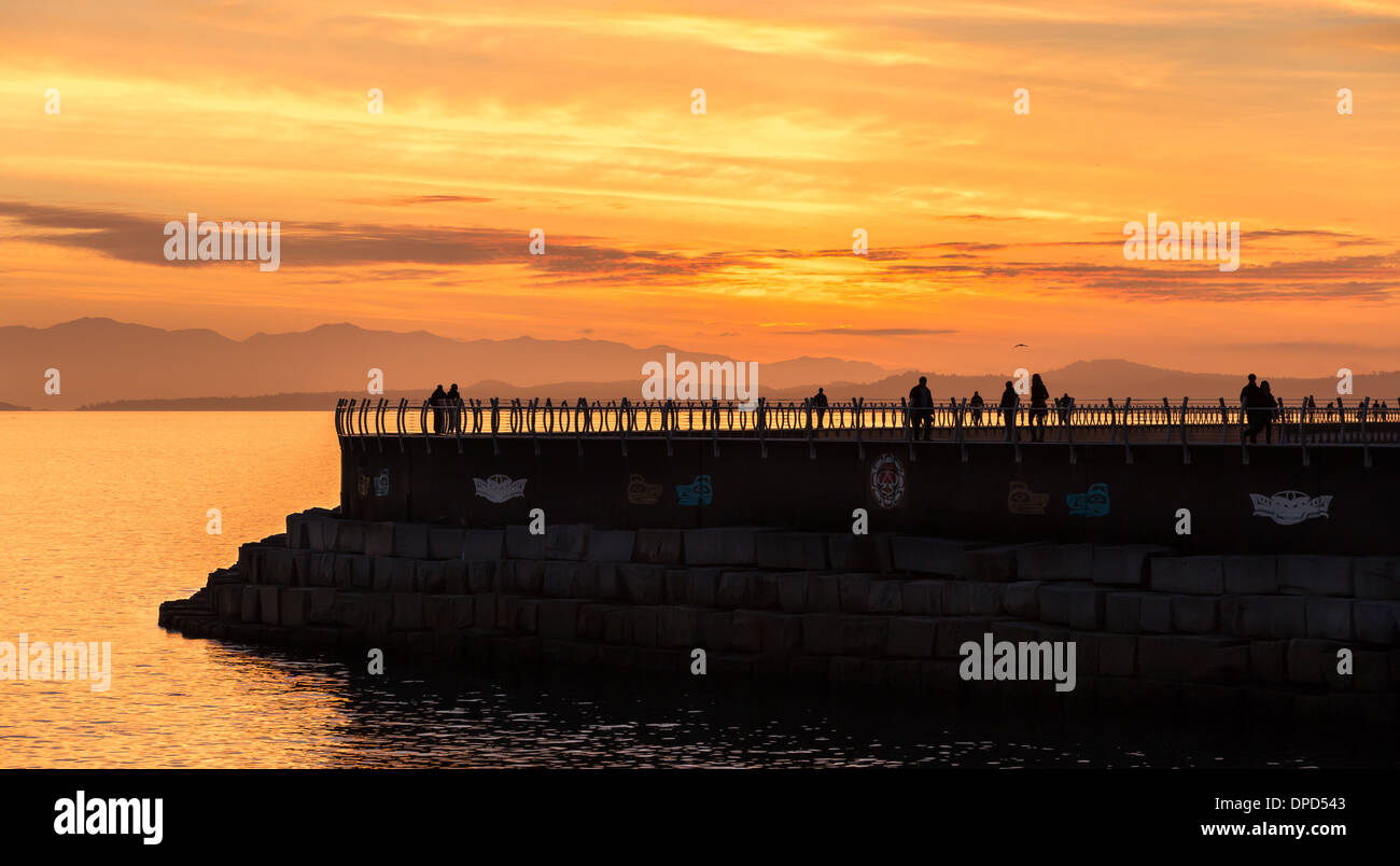 People out for an evening walk enjoy a beautiful sunset over a breakwater in Victoria British Columbia, Canada Stock Photo