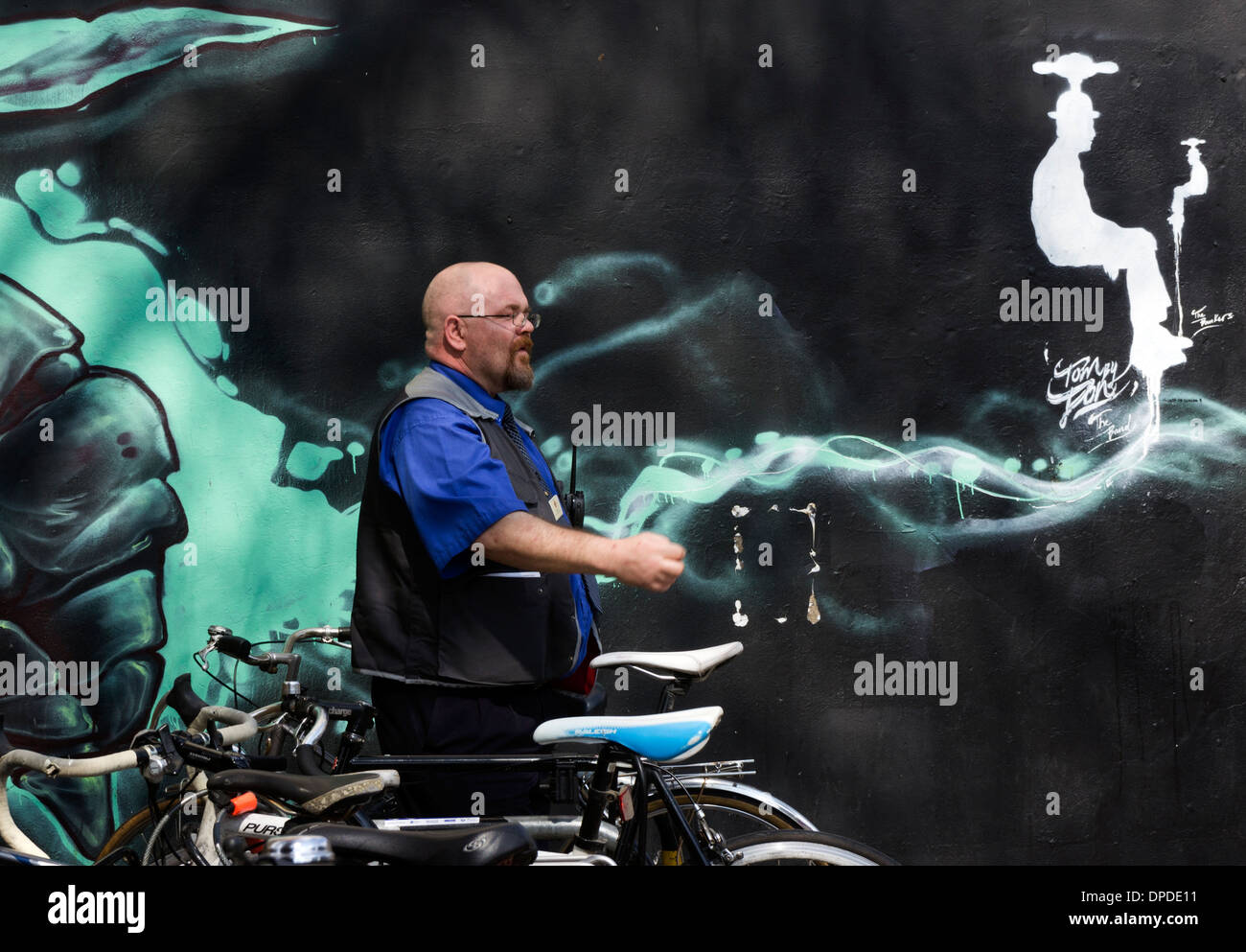 Uniformed man by wall graffiti behind a bicycle parking space Brick Lane area, East London E1 UK Stock Photo