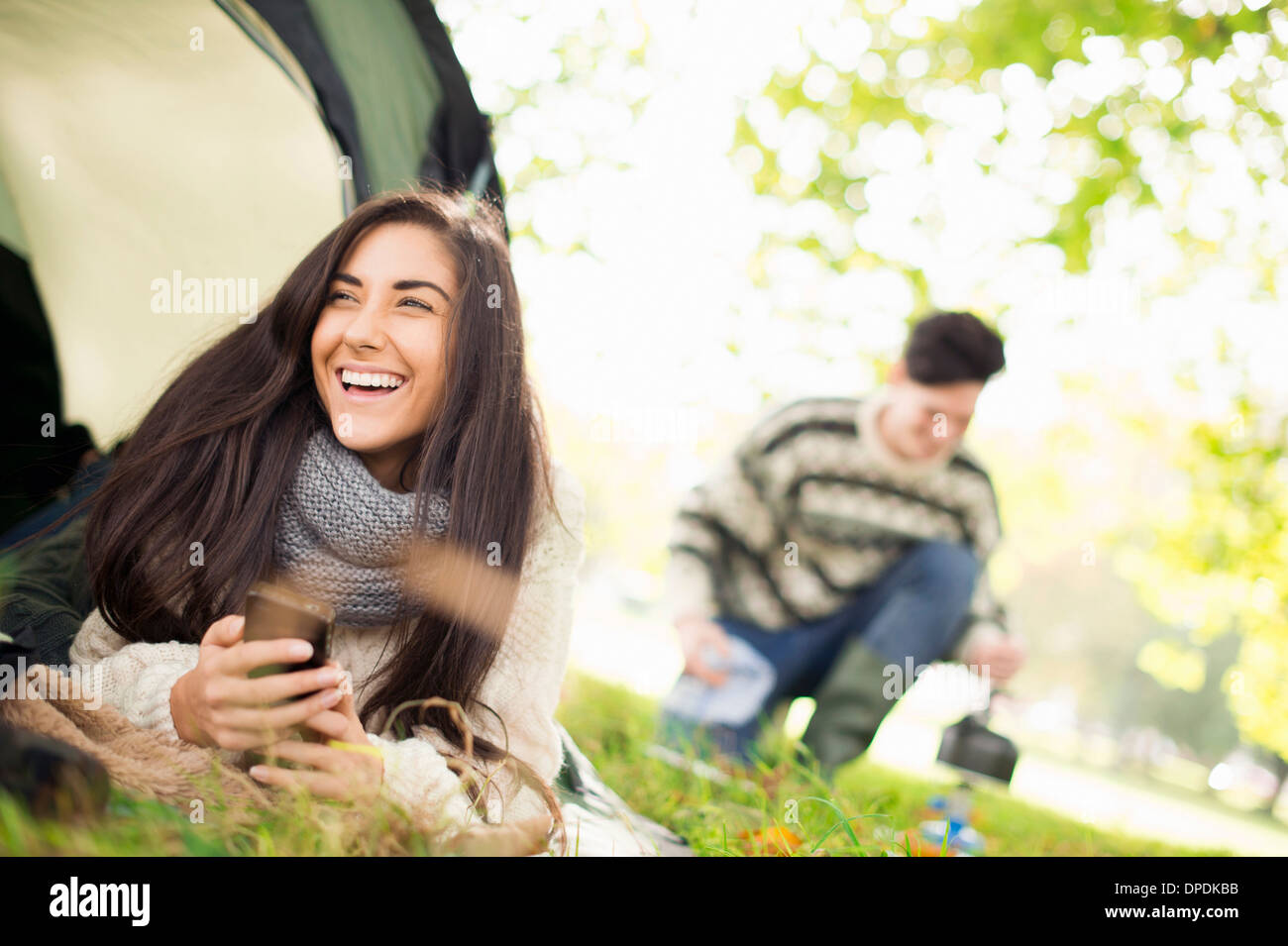 Young woman in tent using smartphone, laughing Stock Photo