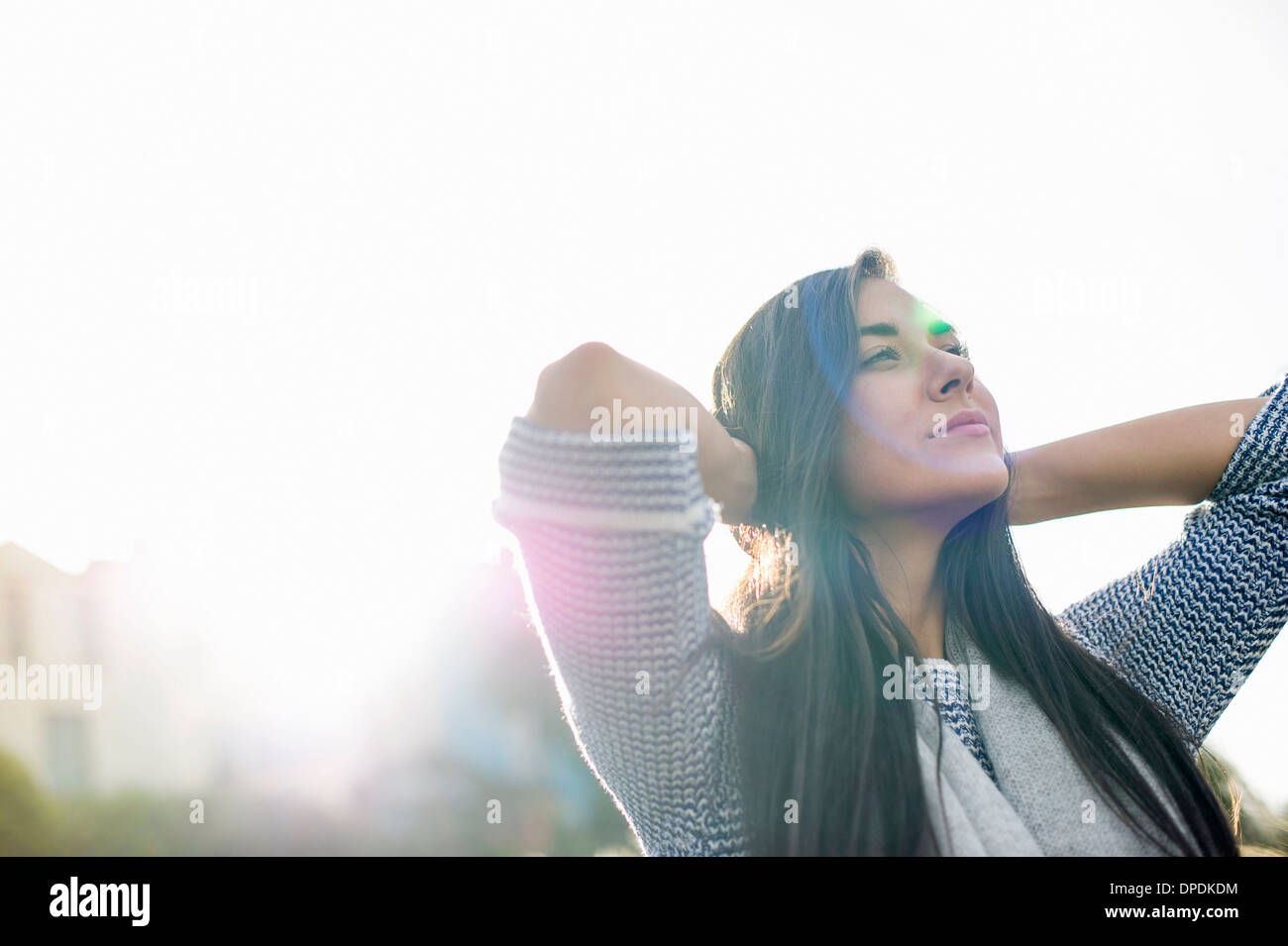 Young woman with hands behind head in sunlight Stock Photo