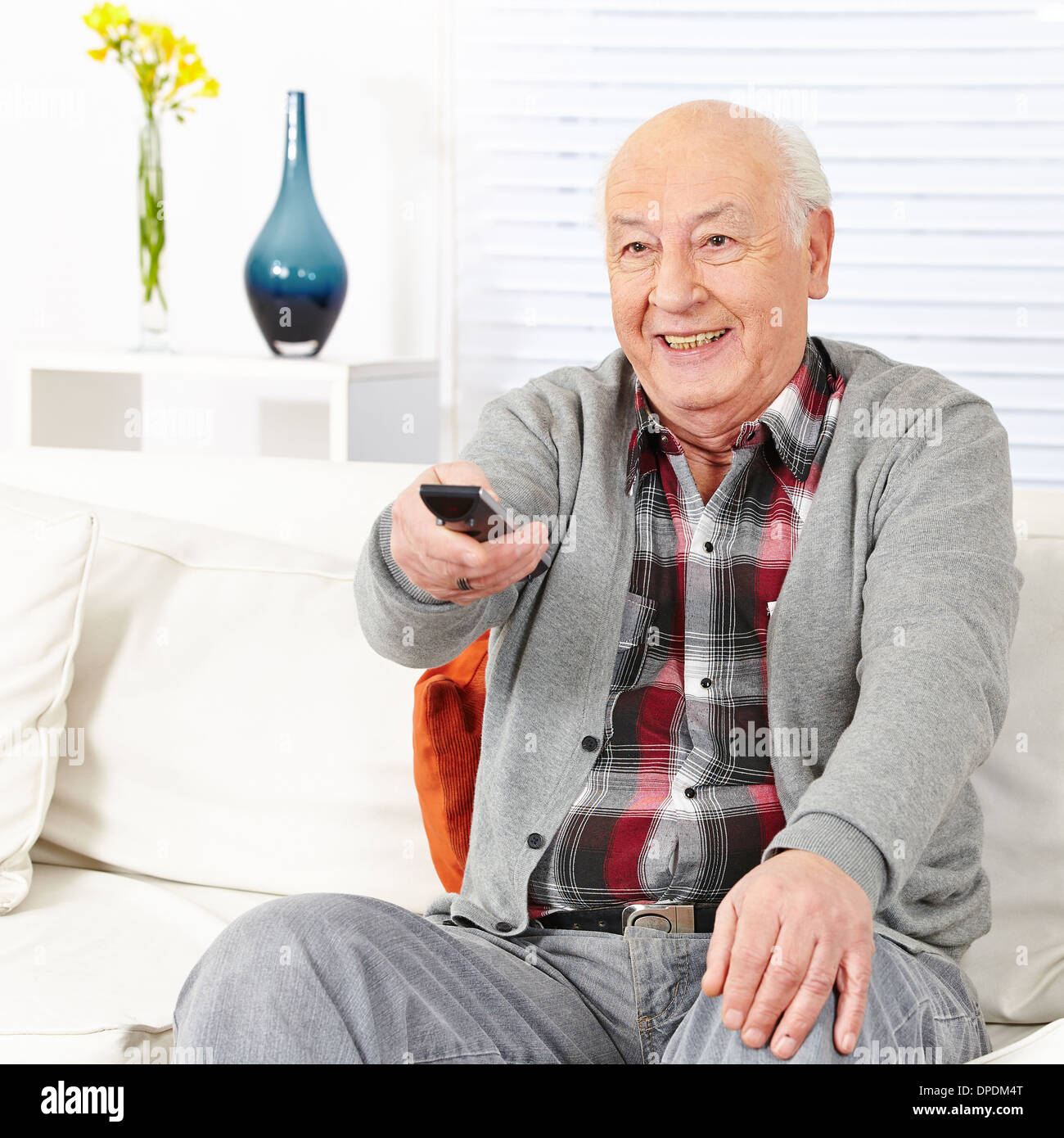 Happy senior citizen man watching TV with remote control Stock Photo
