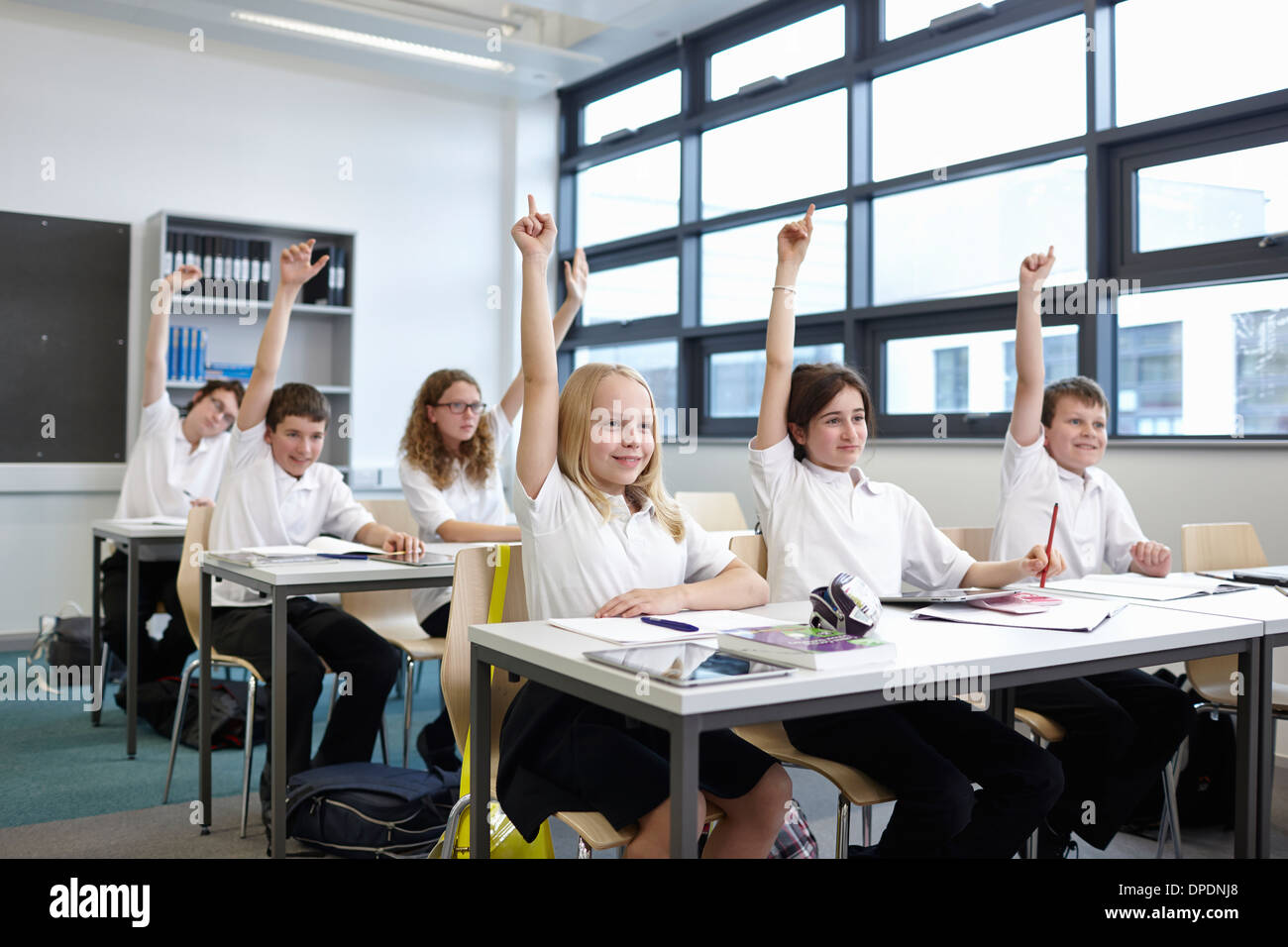 Group of schoolchildren with hands raised in classroom Stock Photo