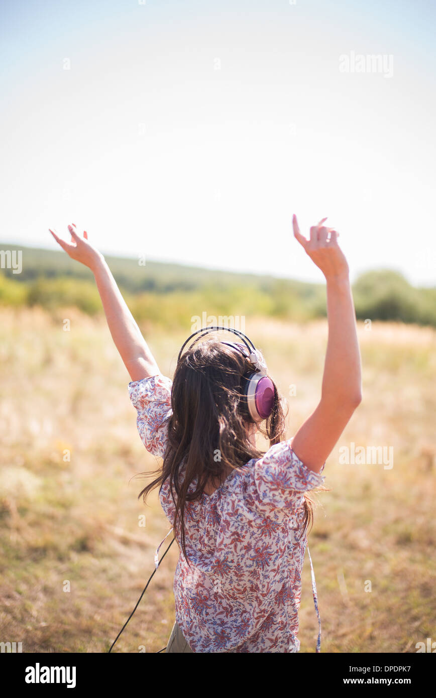 Portrait of mid adult woman dancing in field with arms raised, wearing headphones Stock Photo