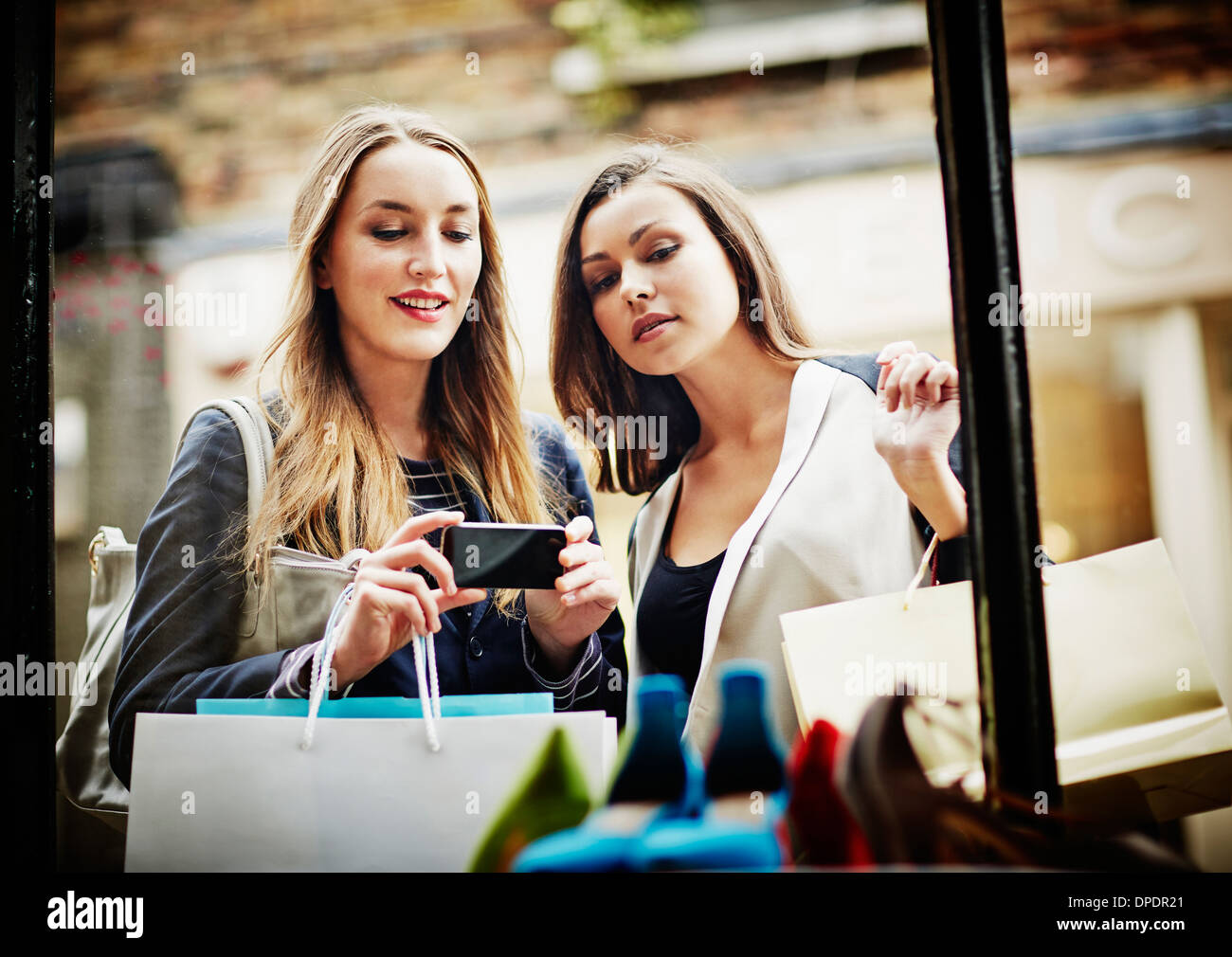 Young women window shopping, taking photograph with smartphone Stock Photo