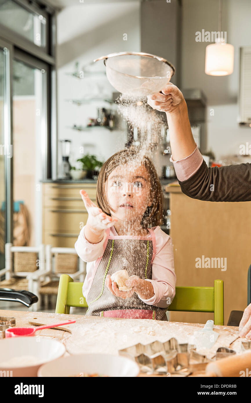 Mother and daughter sieving flour in kitchen Stock Photo