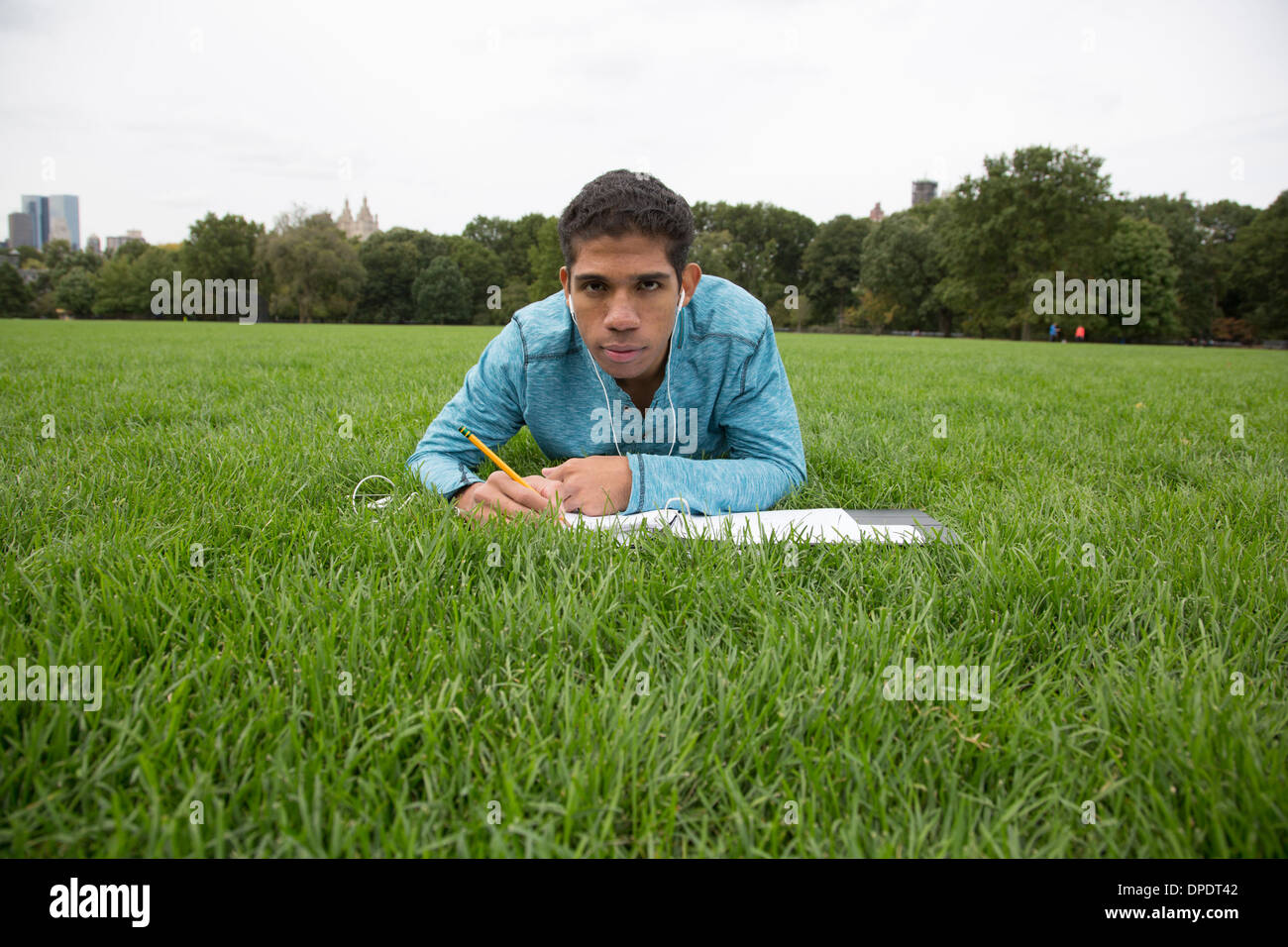 Young man lying on grass doing homework Stock Photo