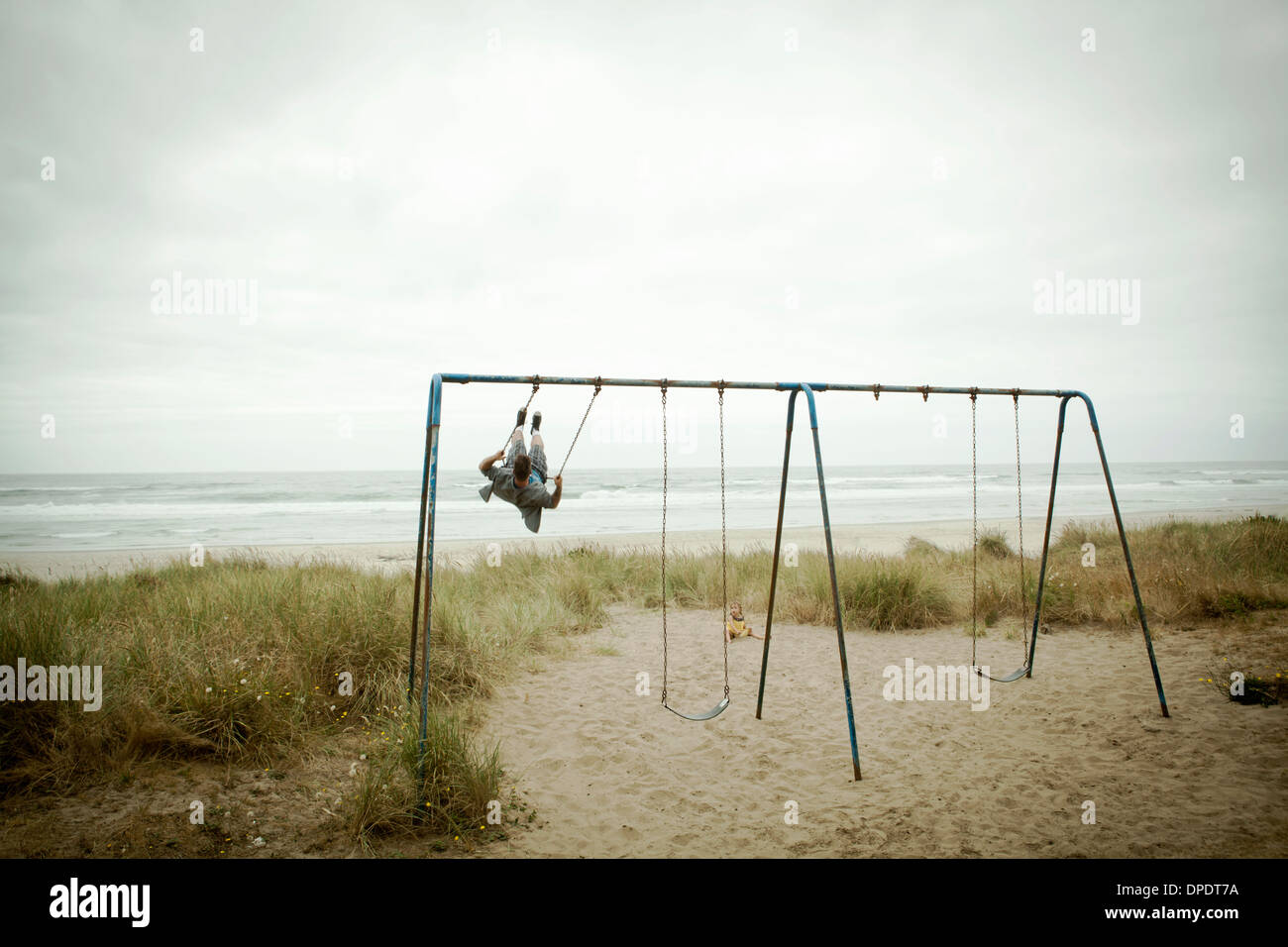 Female toddler watching father on beach swing Stock Photo