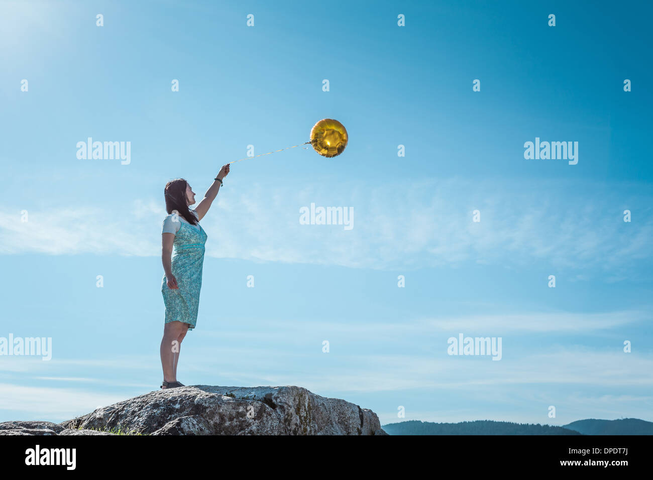 Mature woman standing on rock with golden balloon Stock Photo