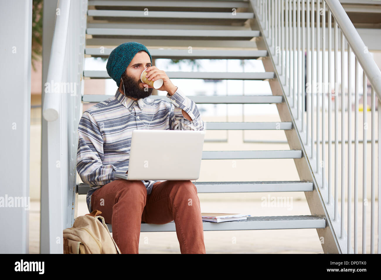 Young bearded hipster student using computer and drinking coffee at university campus Stock Photo