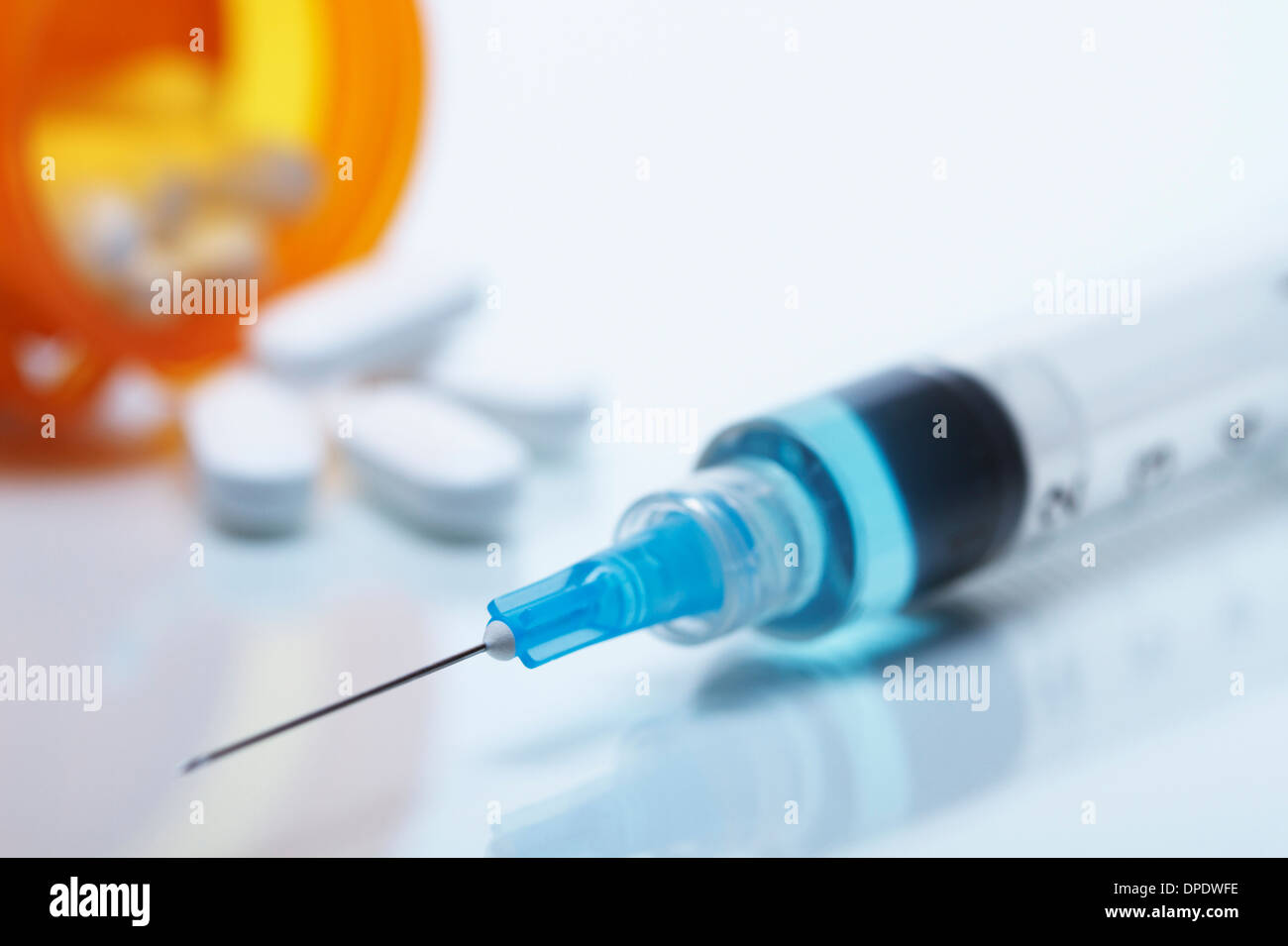 Disposable plastic medical syringe with attached hypodermic needle. Pill bottle and pills in the background Stock Photo