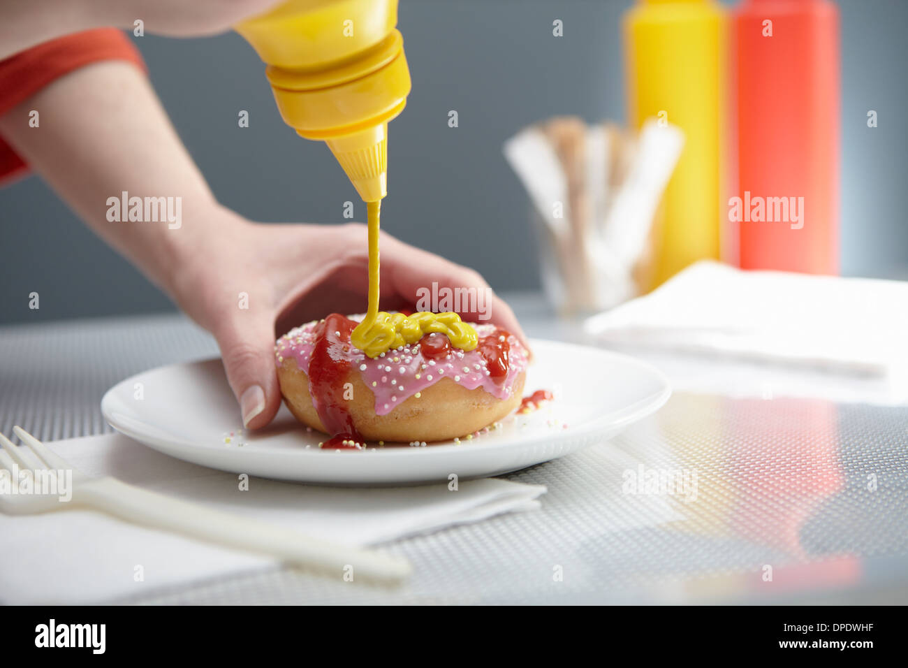 Woman squirting donut with ketchup and mustard Stock Photo