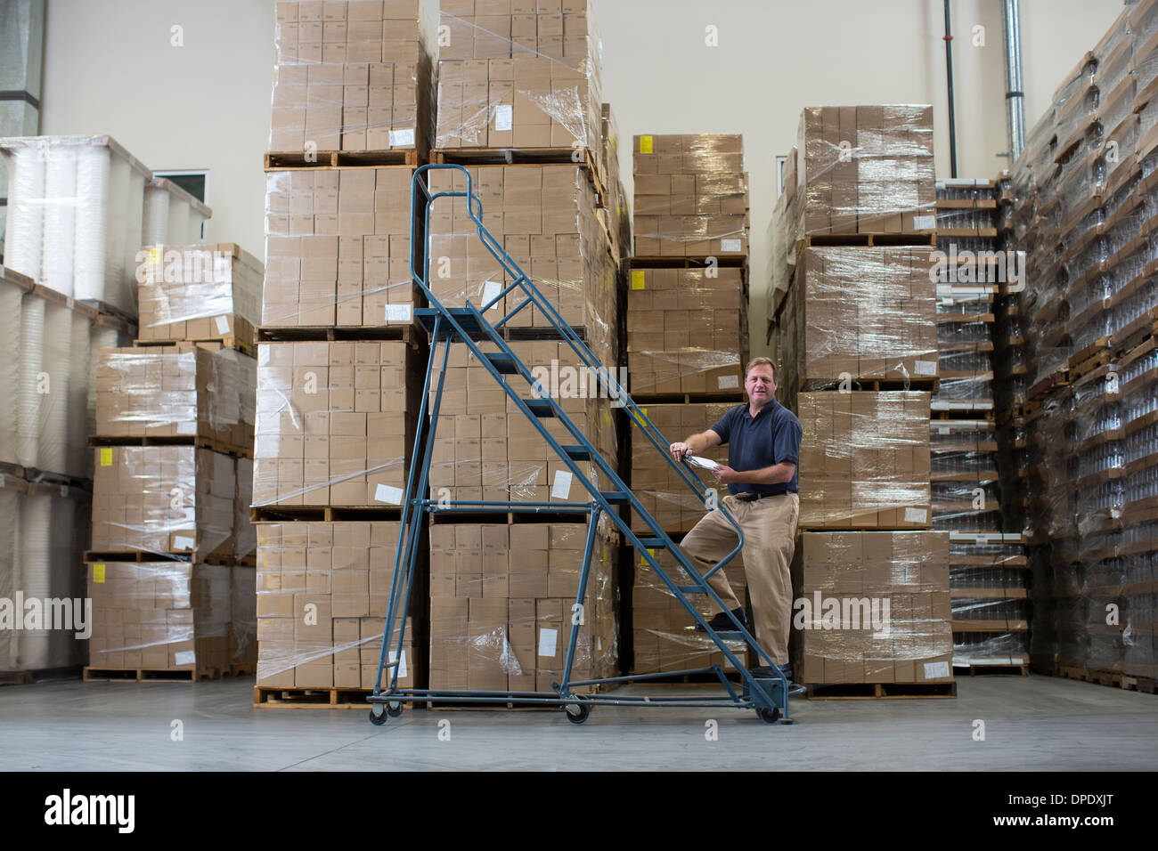 Man on ladders in warehouse with cardboard boxes Stock Photo