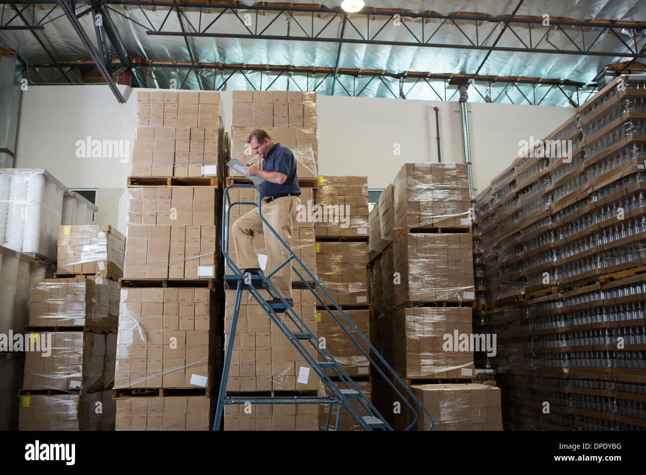 Man on ladders in warehouse with cardboard boxes Stock Photo