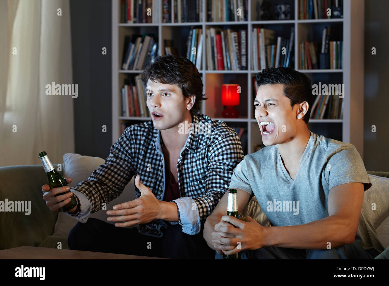 Young men shouting at tv, holding beer bottles Stock Photo