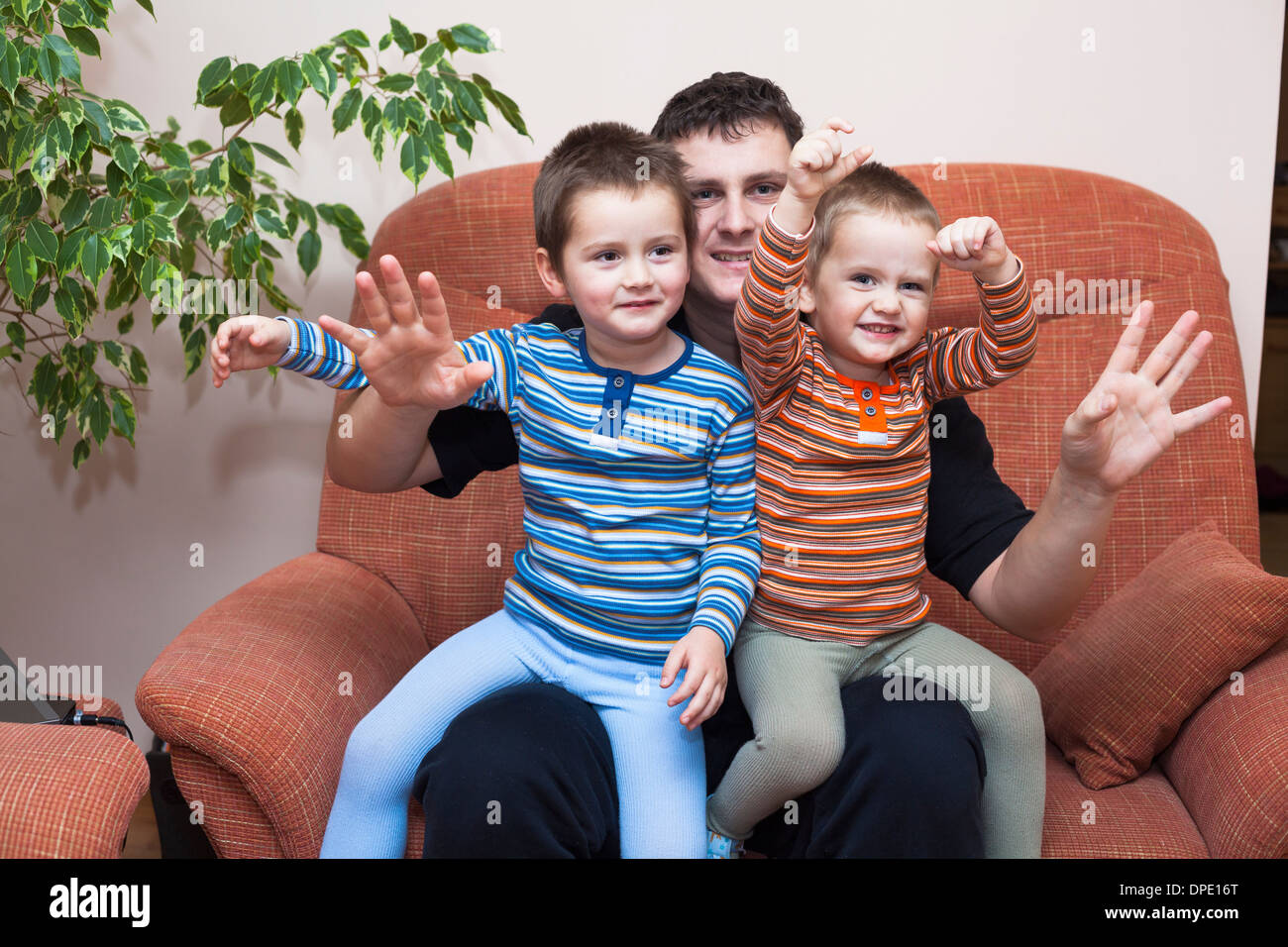 Happy children boys and daddy waving and sitting on sofa at home Stock Photo