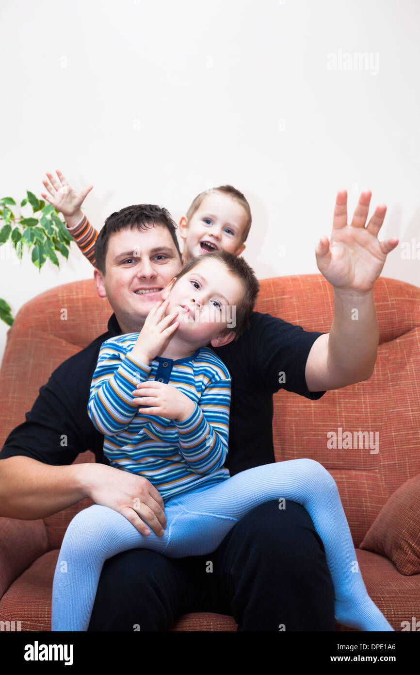 Portrait of happy children boys and daddy waving and sitting on sofa at home Stock Photo