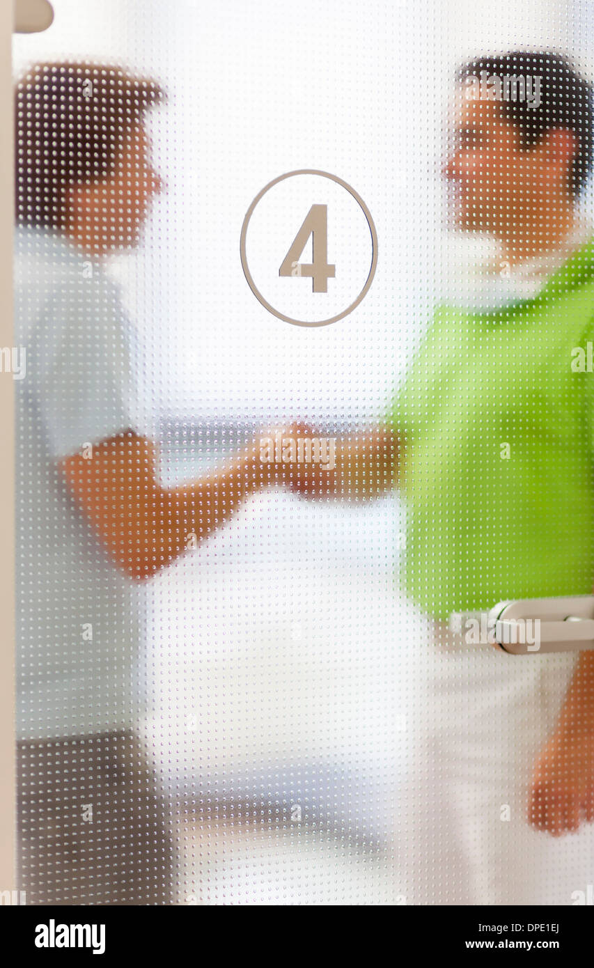 Two men shaking hands behind glass door Stock Photo