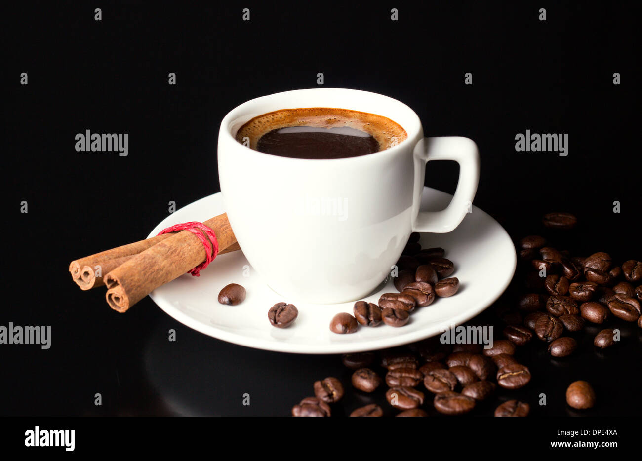 white cup and saucer with coffee beans and cinnamon on black table Stock Photo