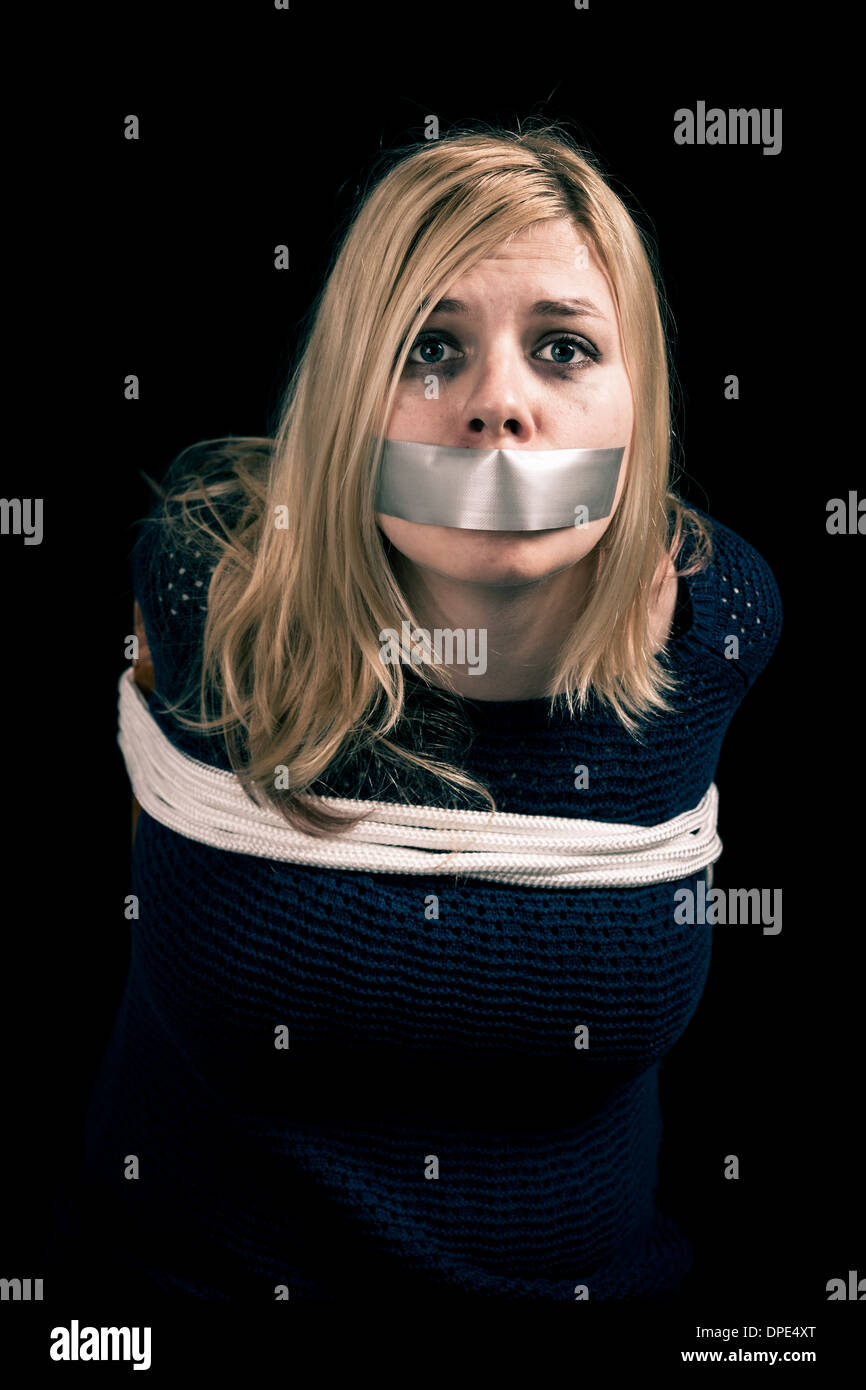 Kidnapped woman hostage with tape over mouth and tied up with rope Stock Photo