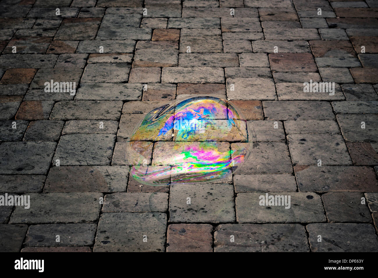 Abstract creative photo of large colorful soap bubble flying over dark pavement background. Stock Photo