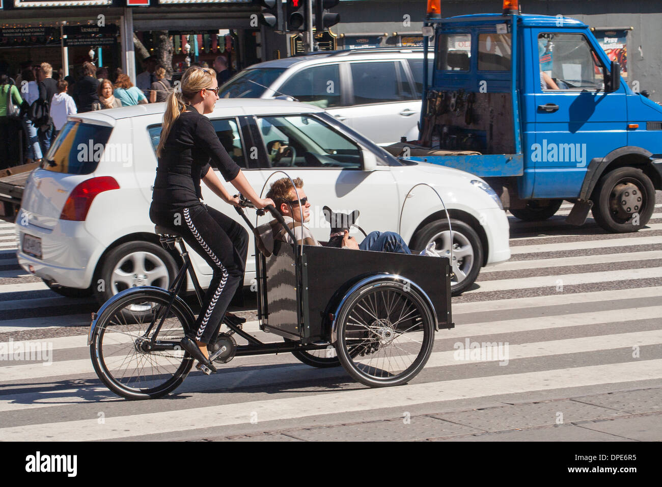 Denmark, Copenhagen, young woman riding a Christiania bike with man and dog as passengers Stock Photo