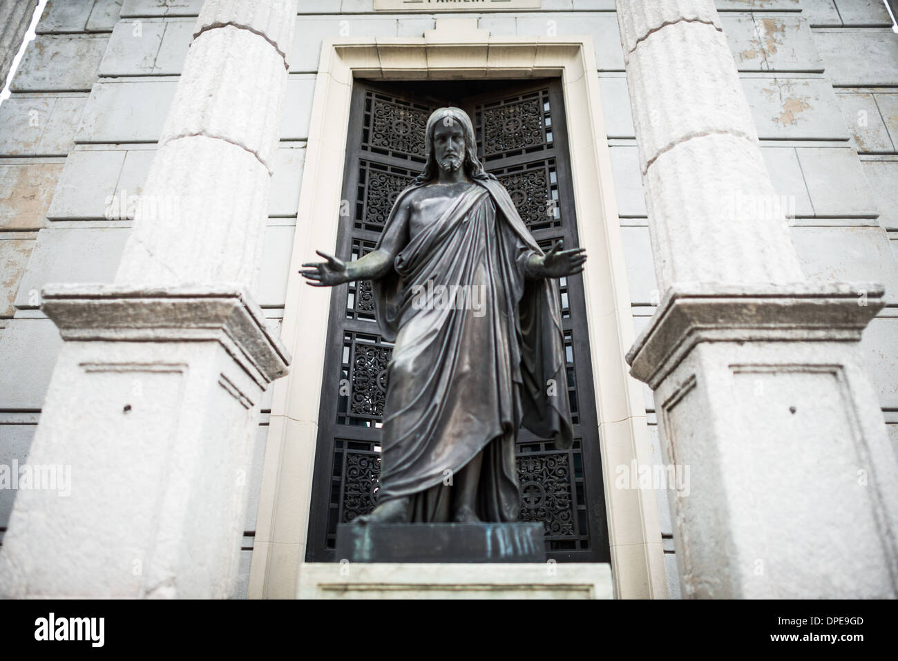 BUENOS AIRES, Argentina — A bronze statue of Jesus stands before a grand mausoleum in Recoleta Cemetery (Cementerio de la Recoleta). This religious sculpture exemplifies the strong Catholic influences in Argentine funerary art. The figure's placement at the entrance of the mausoleum demonstrates the traditional integration of religious iconography in cemetery architecture. Stock Photo